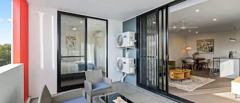 Un appartement moderne doté d’un balcon, d’un coin repas et d’une chambre visible à travers des portes vitrées.
