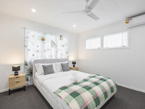 Ein modernes Schlafzimmer mit einem Bett, zwei Nachttischen, einem Deckenventilator und einem Fenster mit Vorhängen.