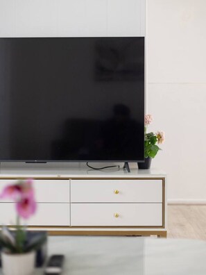 A flat-screen TV on a white cabinet with gold accents, a small potted plant, and a pink flower. - Pet-Friendly & Great Value | Air-Con in Every BR (Sunnybank Hills)