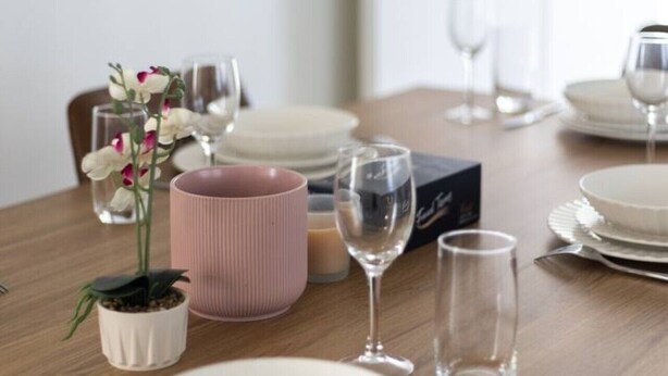 Un tavolo da pranzo apparecchiato con piatti, bicchieri e un vaso rosa con fiori.