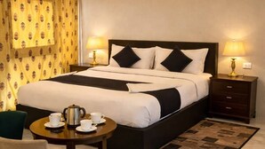 A hotel room with a large bed, bedside tables with lamps, a small round table with cups and a teapot, and a chair. - Elite Family Desert Camp Jaisalmer (Jaisalmer)