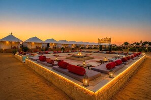 A desert camp with multiple tents, outdoor seating areas with cushions and lanterns, and a central fire feature. - Elite Family Desert Camp Jaisalmer (Jaisalmer)