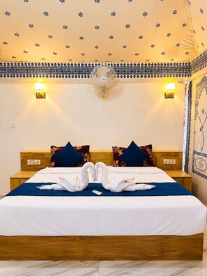 A hotel room with a bed, two bedside tables, a wall-mounted fan, and decorative wall sconces. - Elite Family Desert Camp Jaisalmer (Jaisalmer)