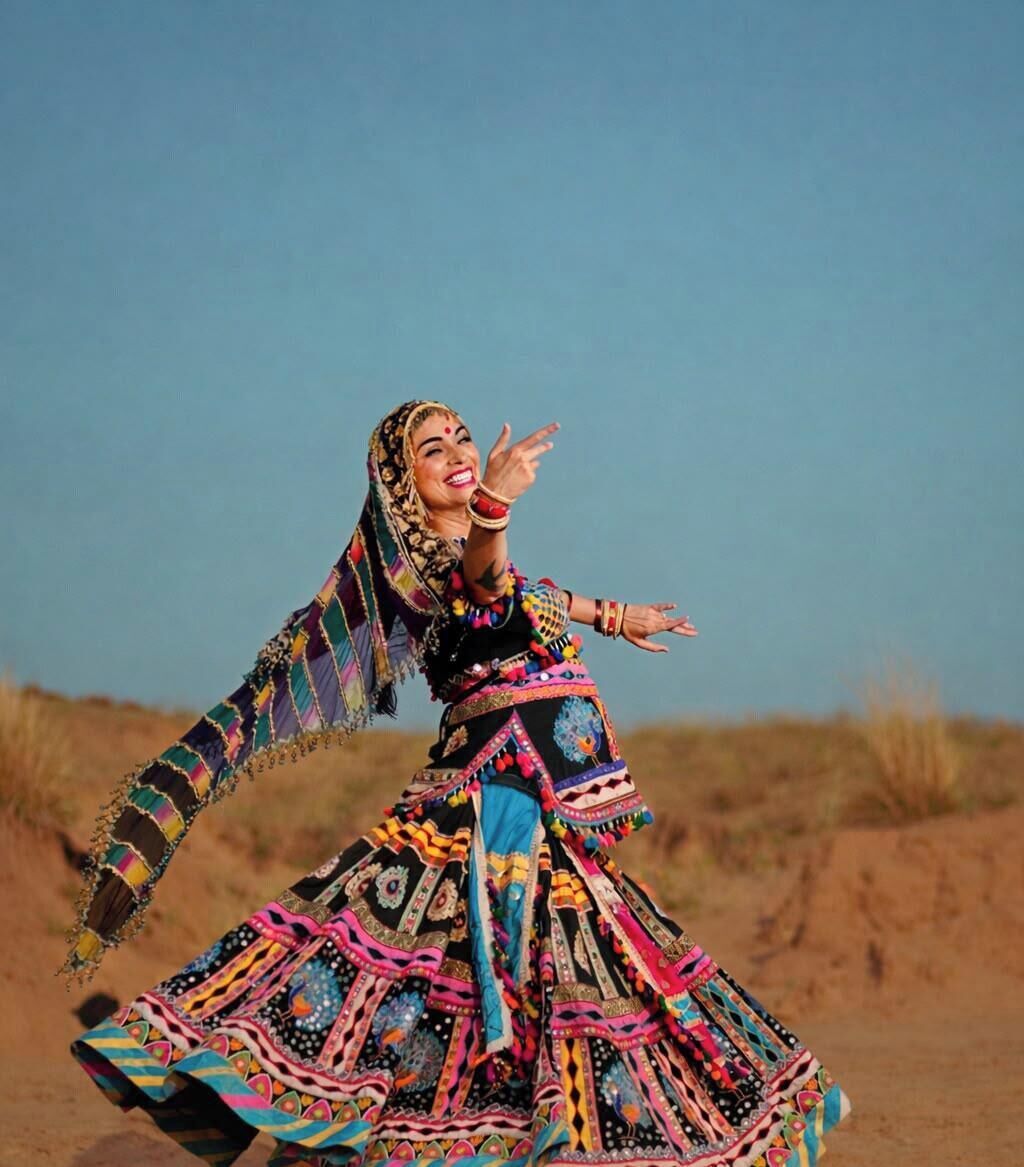 Eine Person in einem farbenfrohen, traditionellen Kleid, die in einer natürlichen Umgebung auftritt.