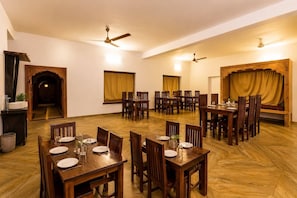 A spacious dining area with multiple tables and chairs, ceiling fans, and a warm ambiance.