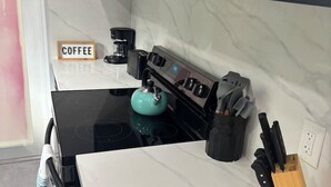 Ett kök med en svart spis, en turkos vattenkokare, en kaffebryggare och ett knivställ.