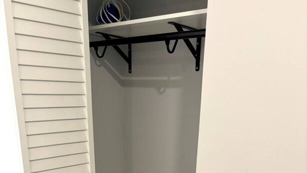 En garderob med en vit dörr, grå väggar och en svart metallstång för att hänga upp kläder.