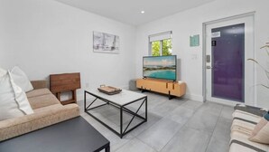 Ett modernt vardagsrum med en soffa, ett soffbord, en tv på ett träställ och en dörr med en lila ram.