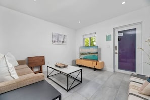 Ein modernes Wohnzimmer mit einer Couch, einem Couchtisch, einem Fernseher auf einem Holzgestell und einer Tür mit violettem Rahmen.