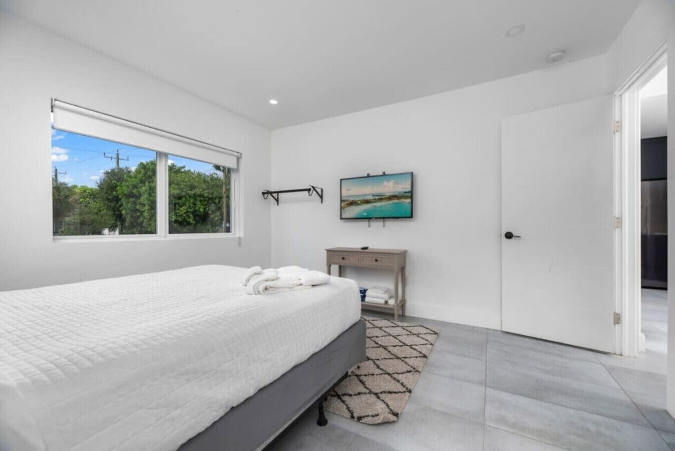 A bedroom with a large bed, a bedside table, a TV, and a window with a view of greenery.