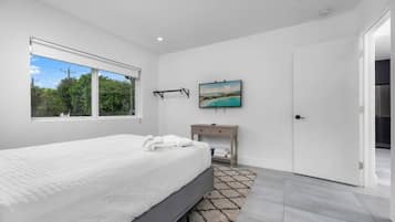 A bedroom with a large bed, a bedside table, a TV, and a window with a view of greenery.