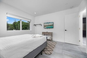 Ein Schlafzimmer mit einem großen Bett, einem Nachttisch, einem Fernseher und einem Fenster mit Blick auf Grünflächen.