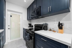 Une cuisine moderne avec des meubles de couleur sombre, un plan de travail blanc et une hotte de cuisine en acier inoxydable.