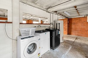 Un lavadero con lavadora, secadora y un cuarto de servicio con pared de ladrillo y tuberías del techo a la vista.