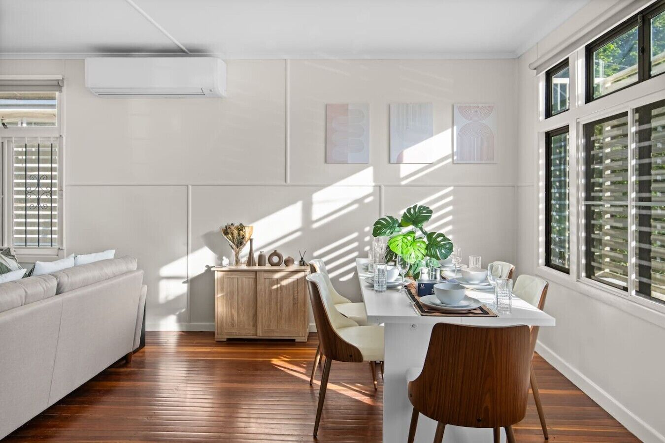 A modern dining area with a wooden dining table, white chairs, and a potted plant.