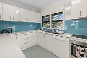 A modern kitchen with white cabinets, a blue backsplash, and a window with a metal grid. - Great Value 5BR Home | Near River & Great Location (Yeronga)