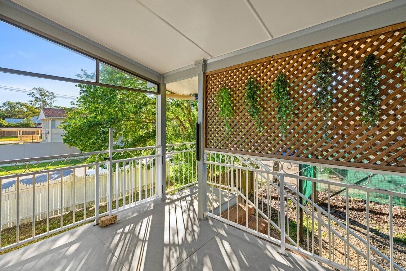A covered balcony with a view of a residential area, a wooden lattice partition, and a metal railing.