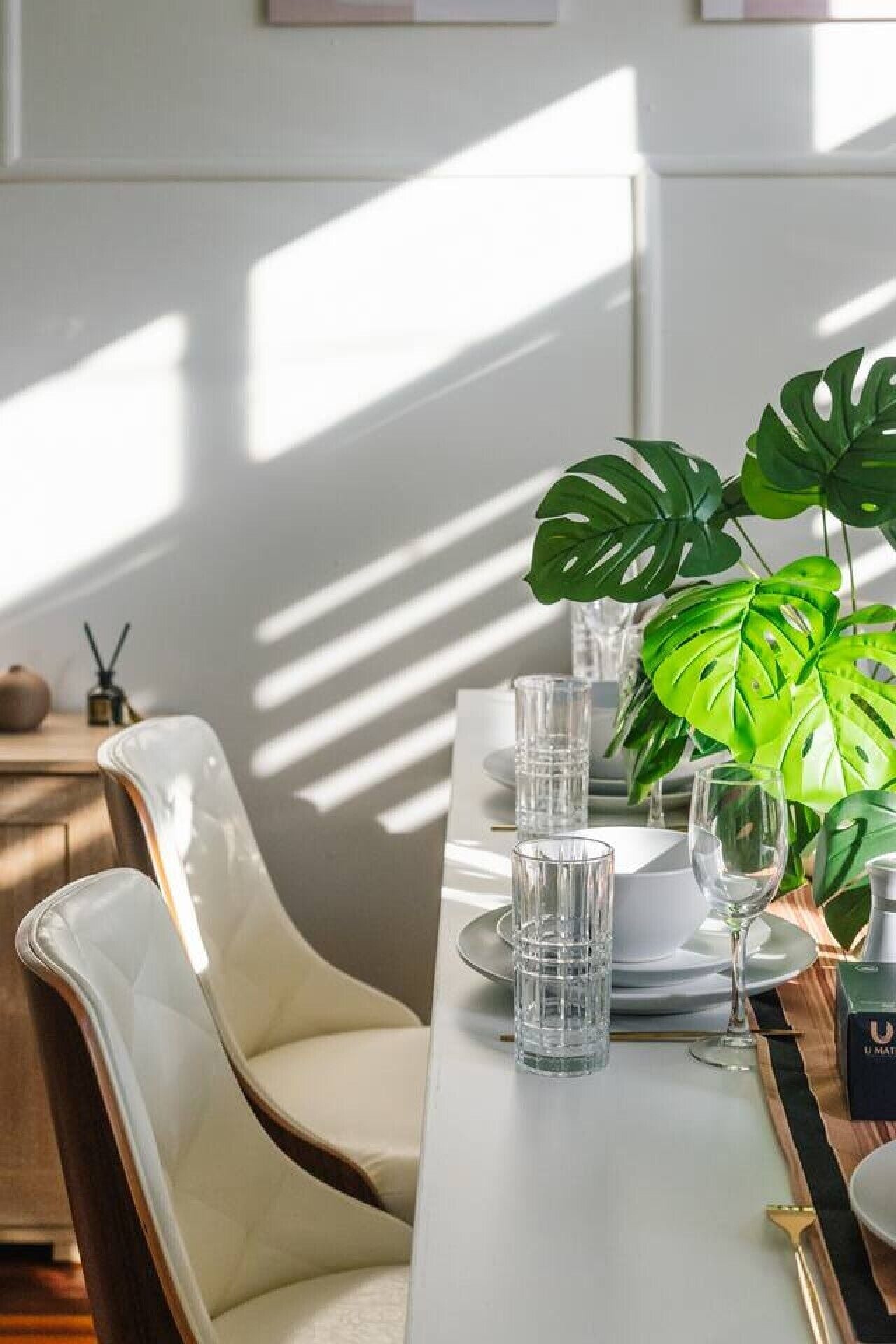 A dining table set with clear glasses, plates, and a wine glass, accompanied by a potted plant.