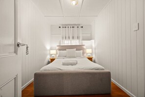 Ein Schlafzimmer mit einem Bett, Nachttischlampen, einem Nachttisch, einer Tür mit Schlüsselbund und einer Deckenleuchte.