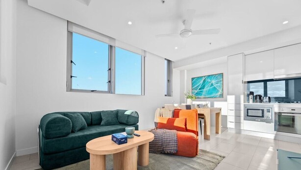 A modern living room with a sofa, a coffee table, and a dining area with a table and chairs. - The Valley 1BR + Sofa Bed | Parking | Pool & Gym (Fortitude Valley)