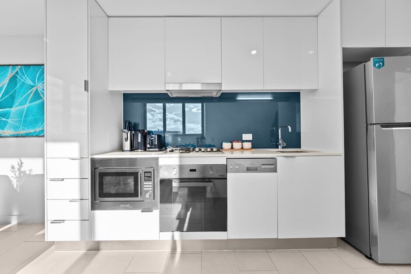 A modern kitchen with white cabinetry, stainless steel appliances, and a blue backsplash.