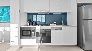 A modern kitchen with white cabinetry, stainless steel appliances, and a blue backsplash. - The Valley 1BR + Sofa Bed | Parking | Pool & Gym (Fortitude Valley)