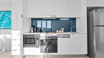 A modern kitchen with white cabinetry, stainless steel appliances, and a blue backsplash.