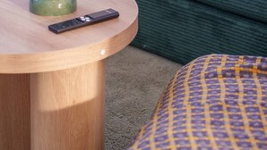 A green sofa with a remote control and a candle on a wooden table. - The Valley 1BR + Sofa Bed | Parking | Pool & Gym (Fortitude Valley)