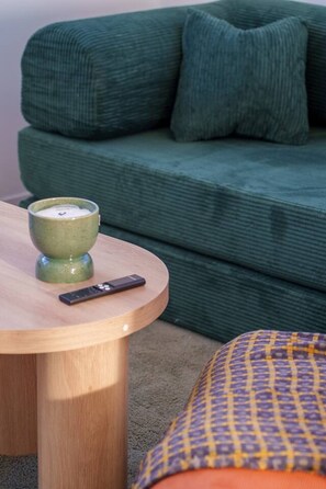 Ein grünes Sofa mit Fernbedienung und einer Kerze auf einem Holztisch.