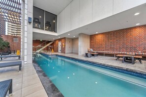 An indoor swimming pool with a brick wall, lounge chairs, and a staircase. - The Valley 1BR + Sofa Bed | Parking | Pool & Gym (Fortitude Valley)