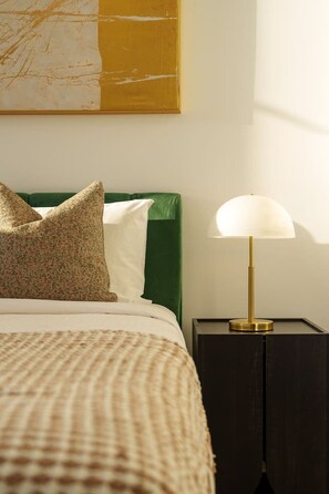 A neatly made bed with a checkered bedspread, a green upholstered headboard, and two pillows. A bedside table with a lamp is visible to the right. - The Valley 1BR + Sofa Bed | Parking | Pool & Gym (Fortitude Valley)