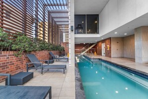An indoor swimming pool with lounge chairs and a brick wall. - The Valley 1BR + Sofa Bed | Parking | Pool & Gym (Fortitude Valley)