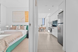 A modern hotel room with a bed, bedside table, and a view into the adjacent kitchen area. - The Valley 1BR + Sofa Bed | Parking | Pool & Gym (Fortitude Valley)