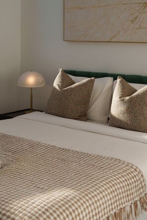 Ein ordentlich bezogenes Bett mit einer karierten Tagesdecke, einer Lampe und Kissen an der Kopfteil.