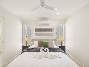 Habitación de hotel con cama, ventilador de techo, equipo de aire acondicionado y dos lámparas de noche.