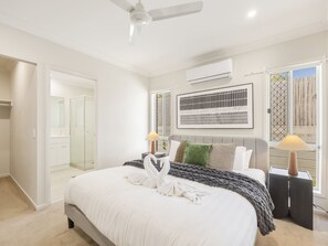 A hotel room with a bed, a ceiling fan, an air conditioning unit, a window with a view, and a nightstand with a lamp. - Stylish 4BR Family Retreat | Peaceful & Convenient (Park Ridge)