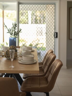 A dining area with a wooden table set for four, surrounded by leather chairs, with a view through a glass door to an outdoor area. - Stylish 4BR Family Retreat | Peaceful & Convenient (Park Ridge)