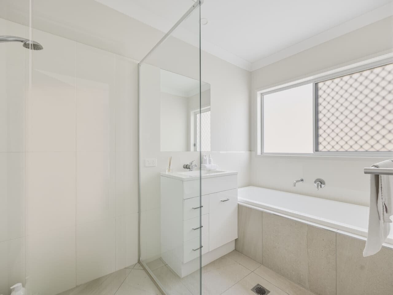 A modern bathroom with a glass shower enclosure, a white vanity with a mirror, and a bathtub.