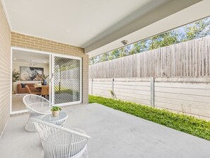 A covered patio with a concrete floor, white wicker furniture, and a wooden fence. - Stylish 4BR Family Retreat | Peaceful & Convenient (Park Ridge)