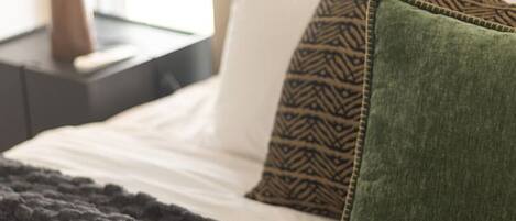 A bed with a dark blanket, a pillow with a geometric pattern, and a green pillow.