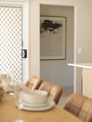 A dining area with a table set for four, a door with a mesh screen, and a framed abstract painting on the wall. - Stylish 4BR Family Retreat | Peaceful & Convenient (Park Ridge)