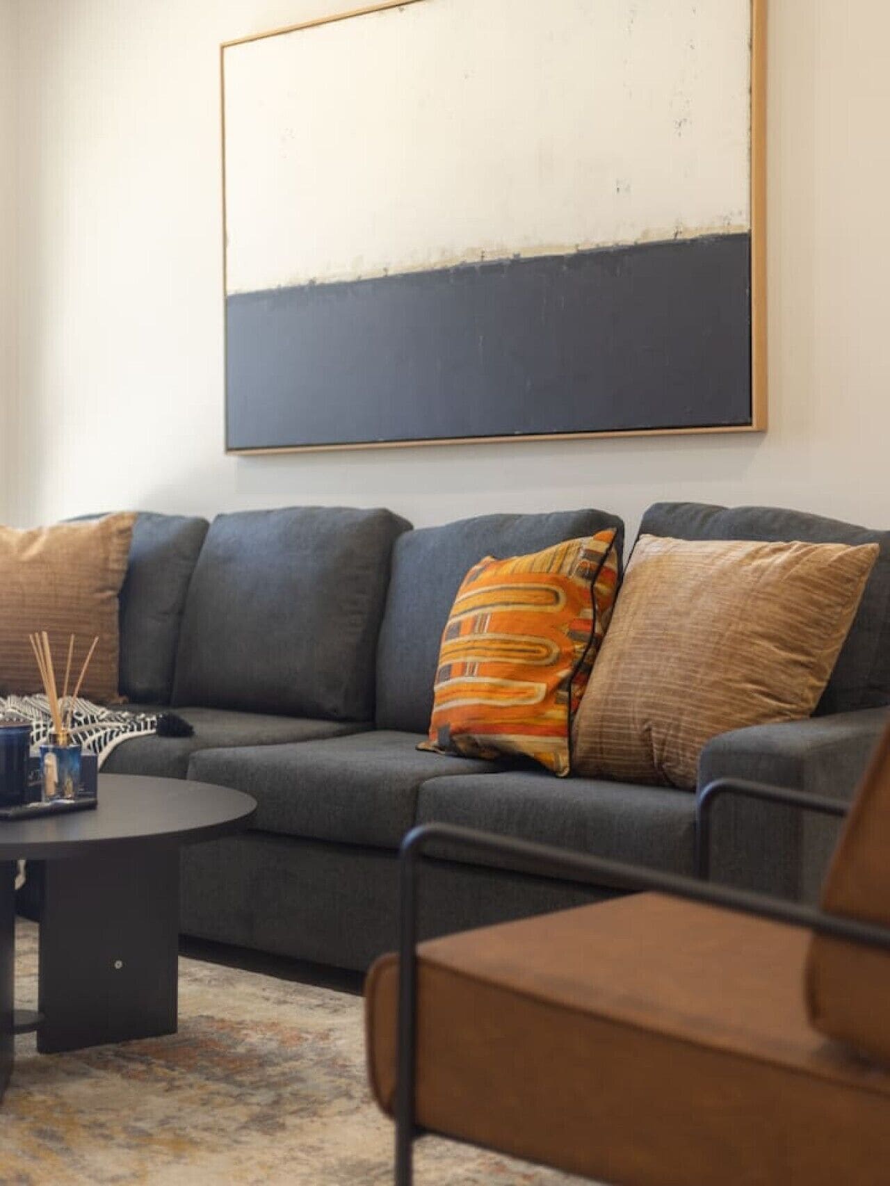 A modern living room with a grey sofa, a round coffee table, and a large abstract painting on the wall.