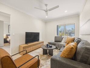 A modern living room with a flat-screen TV, a grey sofa, a coffee table, and a ceiling fan. - Stylish 4BR Family Retreat | Peaceful & Convenient (Park Ridge)