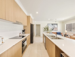 A modern kitchen with a central island, a dining area with a sofa, and a view of the living room. - Stylish 4BR Family Retreat | Peaceful & Convenient (Park Ridge)