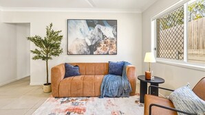 Ett vardagsrum med en soffa, ett soffbord, en lampa, en tavla och en krukväxt.