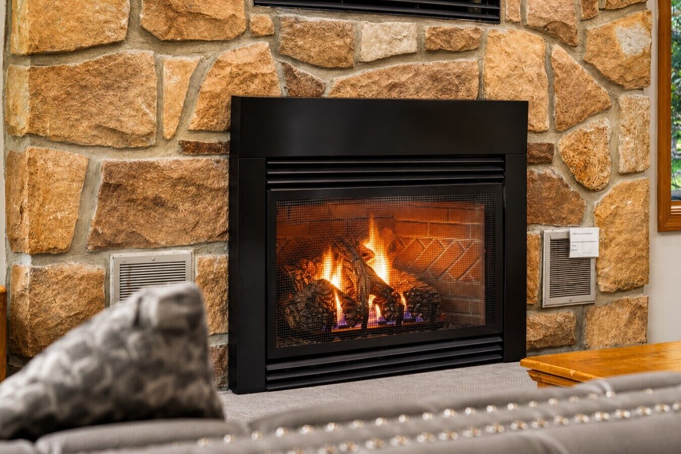 A fireplace with a stone wall backdrop, a sofa with a patterned throw, and a small wooden table.