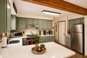 A modern kitchen with green cabinets, stainless steel appliances, and a central island with a candle and plants. - Harmony Pines | Hot Tub & Beach Access (Lake Harmony)