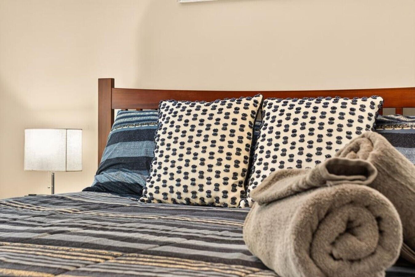 A bed with a striped bedspread, two patterned pillows, and a rolled towel.