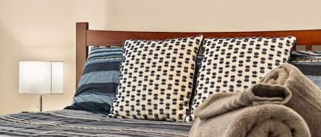 A bed with a striped bedspread, two patterned pillows, and a rolled towel.
