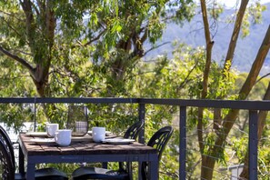 An outdoor dining area with a table set for two, surrounded by greenery and overlooking a mountainous landscape. - Rose Creek Chalet: Cosy 2BR w/ Resort Facilities, Crackenback Resort NSW (Crackenback)